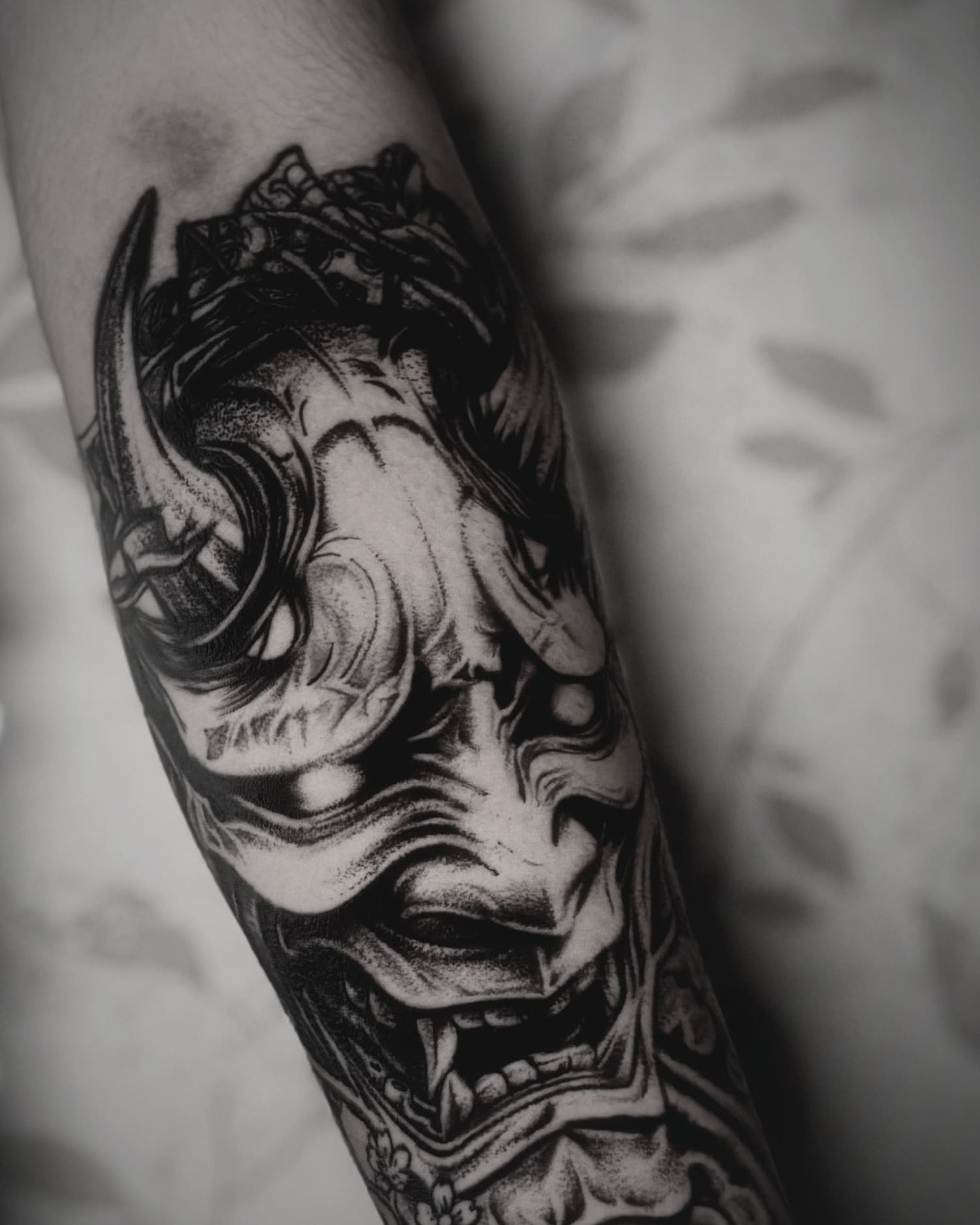Hannya mask worked in black and grey down a forearm, with wave and wind-barb detailing around it