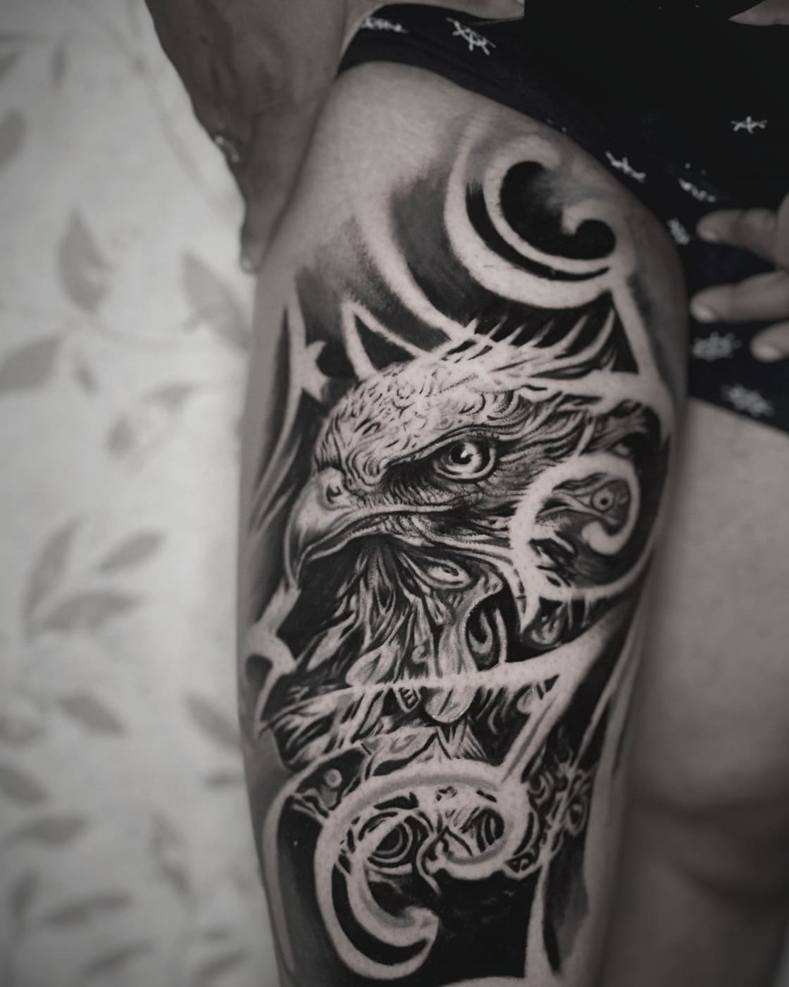 Eagle in packed blackwork on a thigh, framed by ornamental scrollwork and chiselled negative space